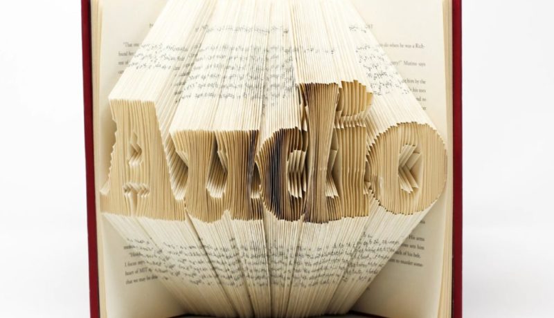 Um livro aberto apoiado em pé em uma superfície branca, as páginas estão dobradas de maneira a formarem a palavra Audio.