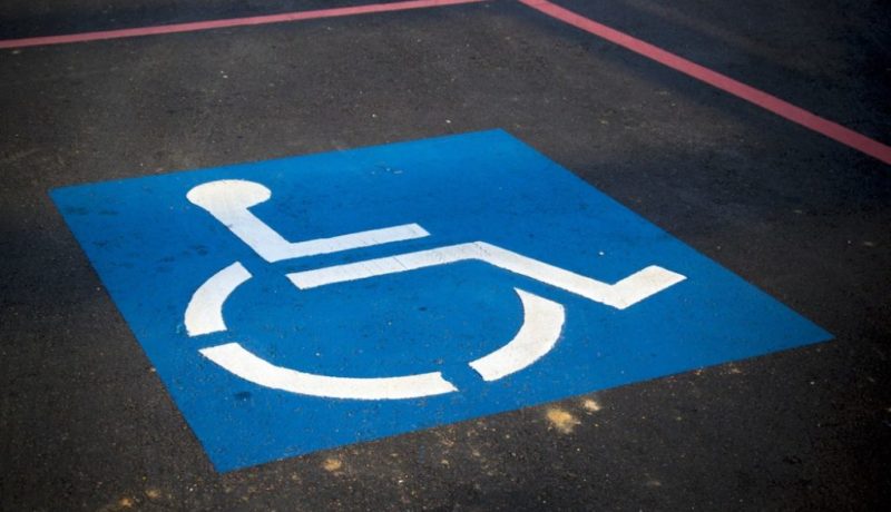 Chão de asfalto com linhas vermelhas demarcando uma vaga para carros. No chão está pintado o símbolo internacional de acesso, um quadrado azul com um boneco branco cadeirante no centro.
