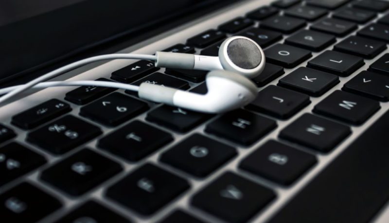 Foto de um fone de ouvido branco sobre um teclado de notebook.