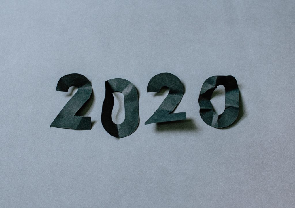 Quatro pedaços de papel preto recortados para formar os números de 2020 sobre um fundo cinza.