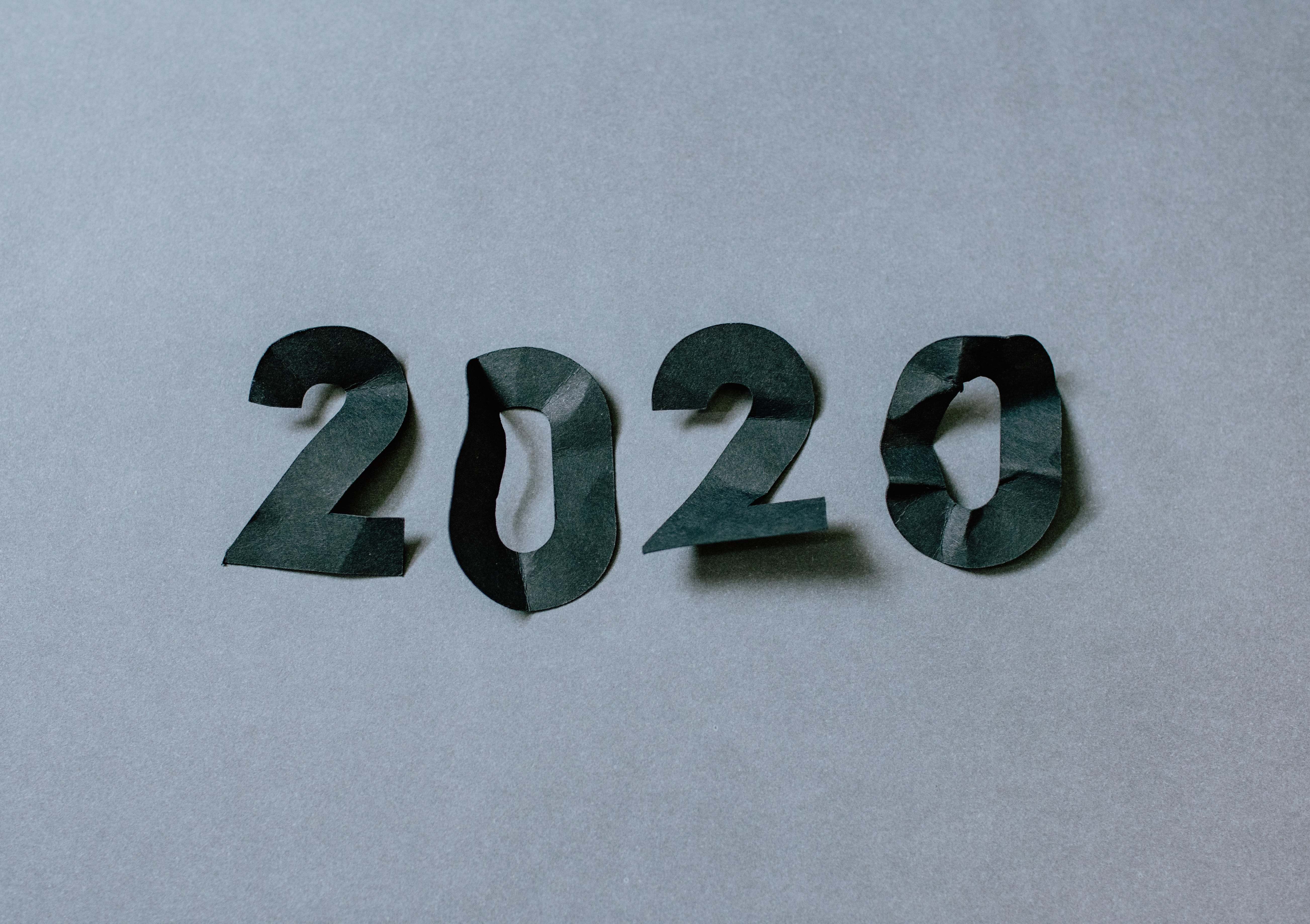 Quatro pedaços de papel preto recortados para formar os números de 2020 sobre um fundo cinza.